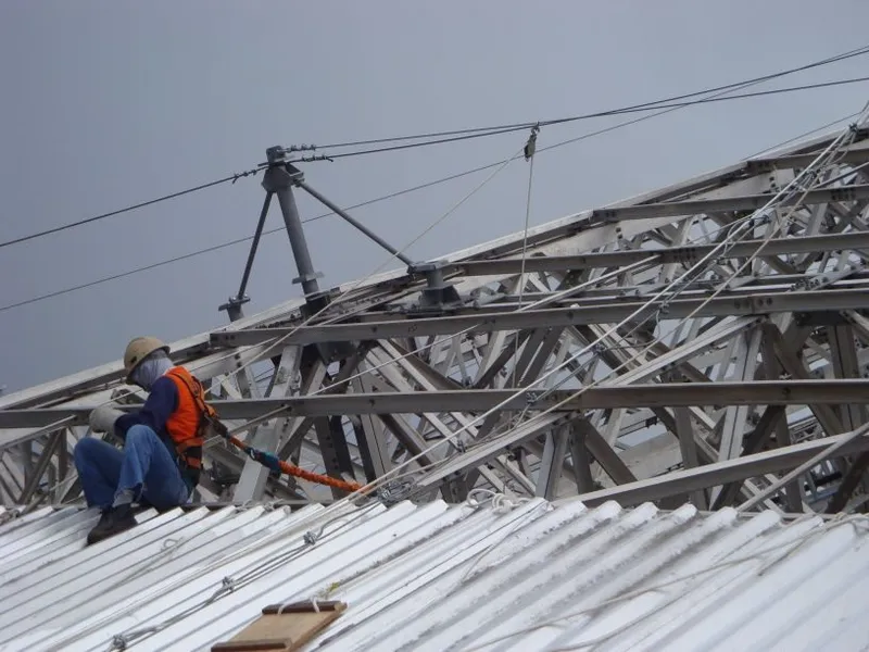 Profissional com cinto de segurança e capacete realizando montagem sobre cobertura metálica treliçada