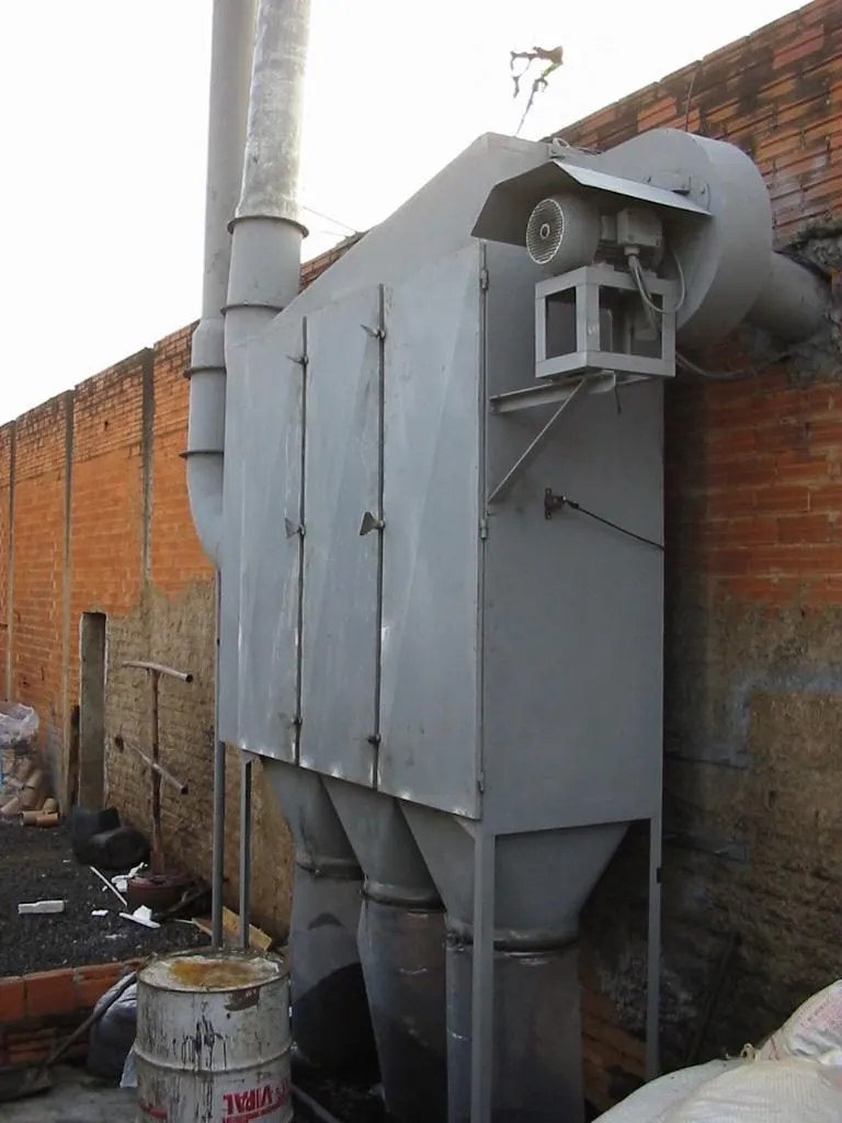 Filtro coletor de pó metálico com motor exaustor no topo, instalado junto a muro em área externa