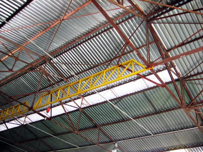 Viga treliçada amarela de ponte rolante instalada sob cobertura metálica de galpão industrial