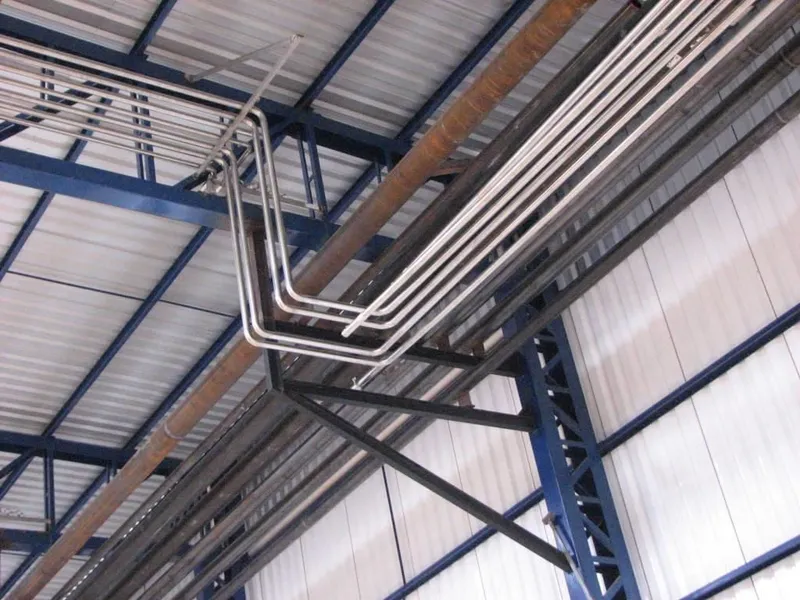 Tubulações em aço inoxidável fixadas em suportes na estrutura metálica da cobertura de galpão