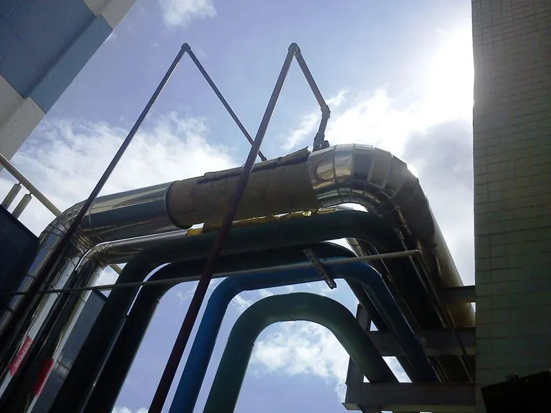 Tubulações industriais com isolamento térmico e revestimento em alumínio instaladas entre edifícios