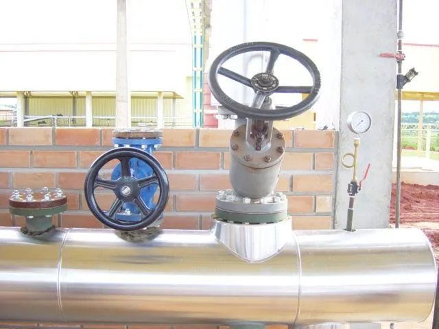 Detalhe de válvulas industriais e manômetro instalados em tubulação com isolamento em alumínio